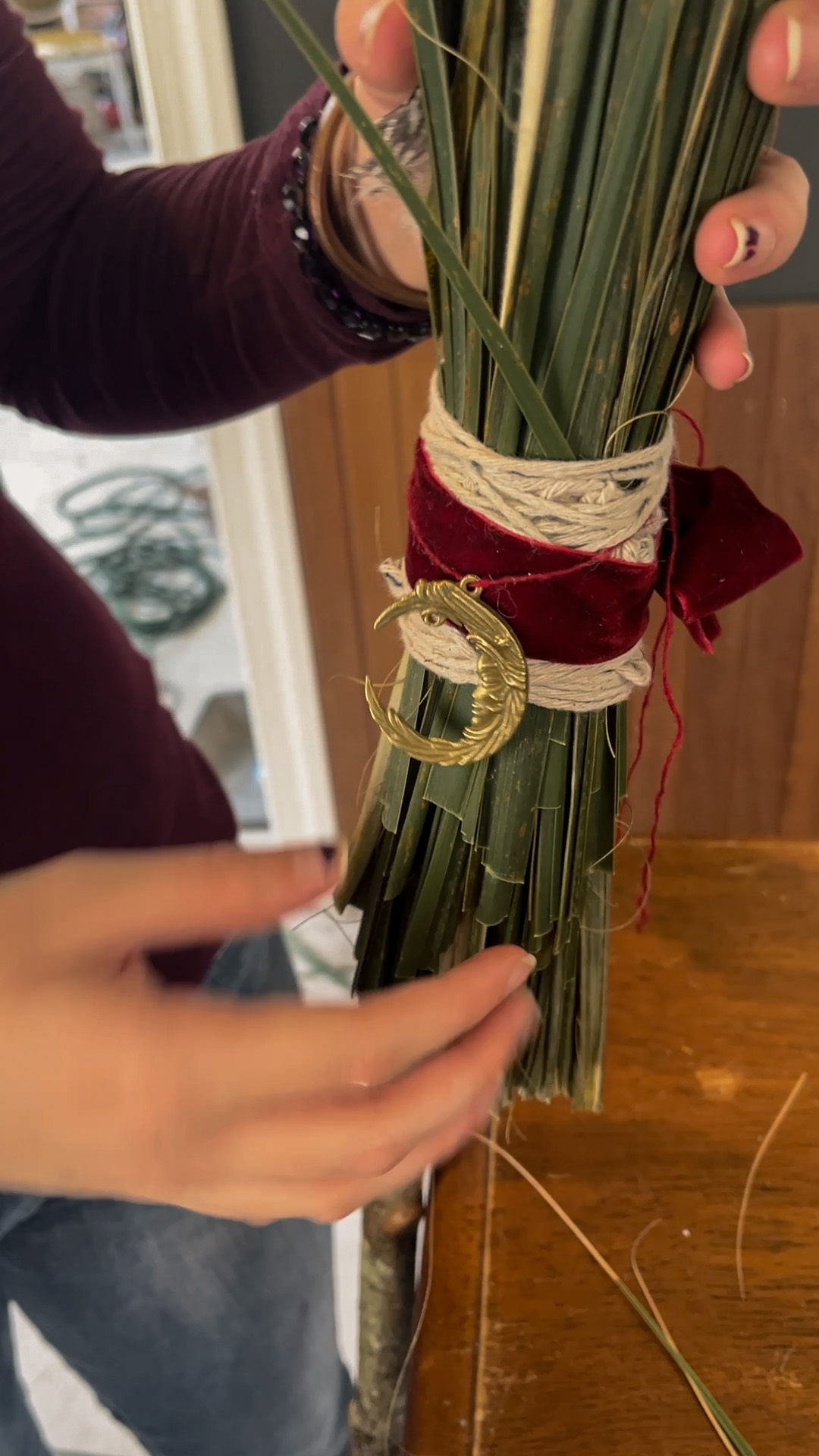 Hands assembling a handmade broom with palmetto, twine and burgundy velvet at the Blackwood Broom Works workshop.