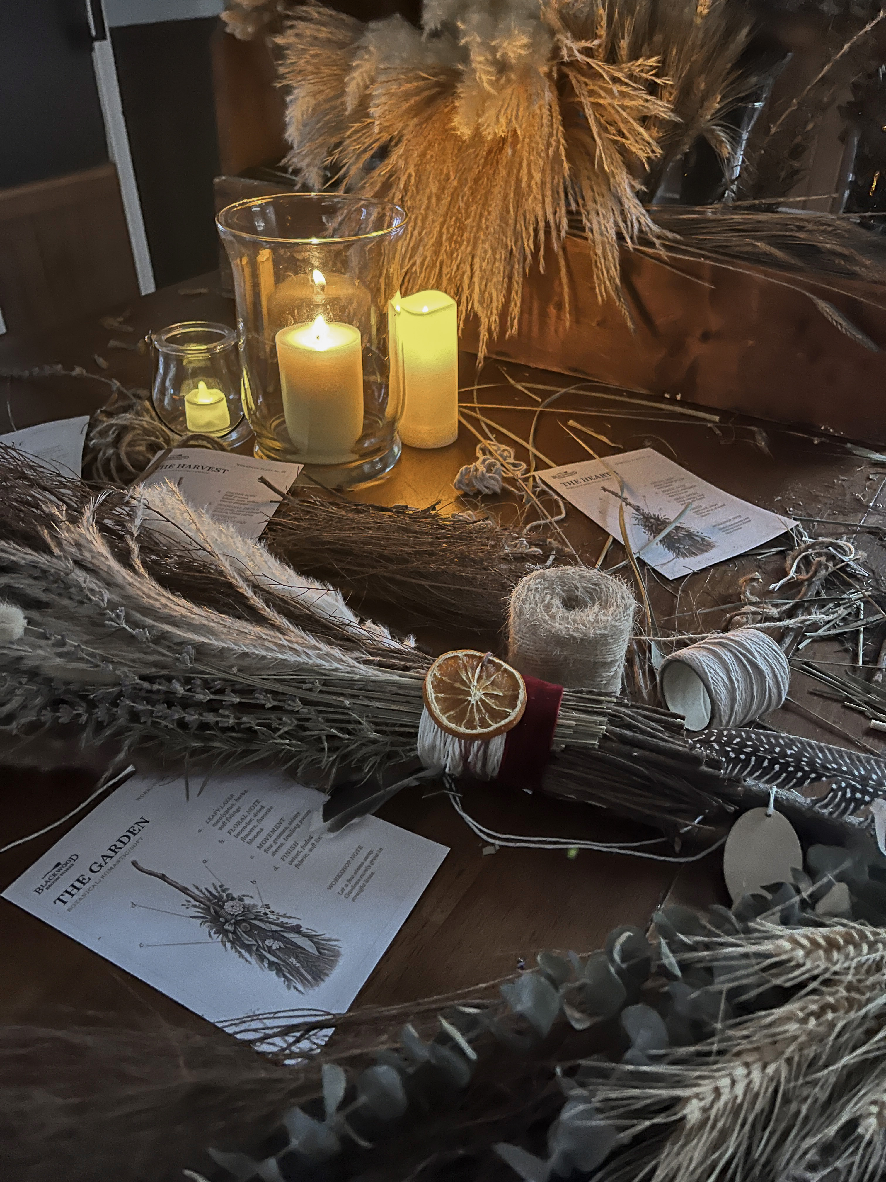 Broom-making supplies, dried grasses and candles spread across the Blackwood workshop table