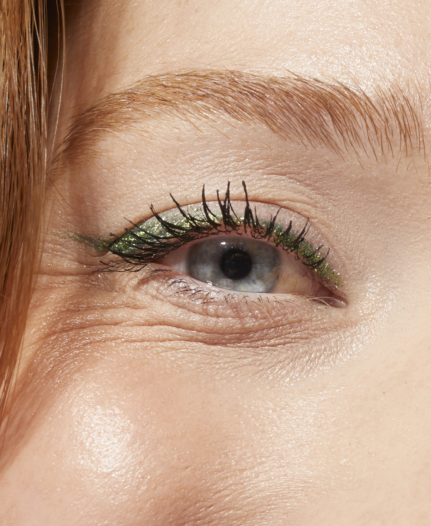Gros plan sur un œil maquillé de paillettes vertes, grain de peau naturel, retouche beauté
