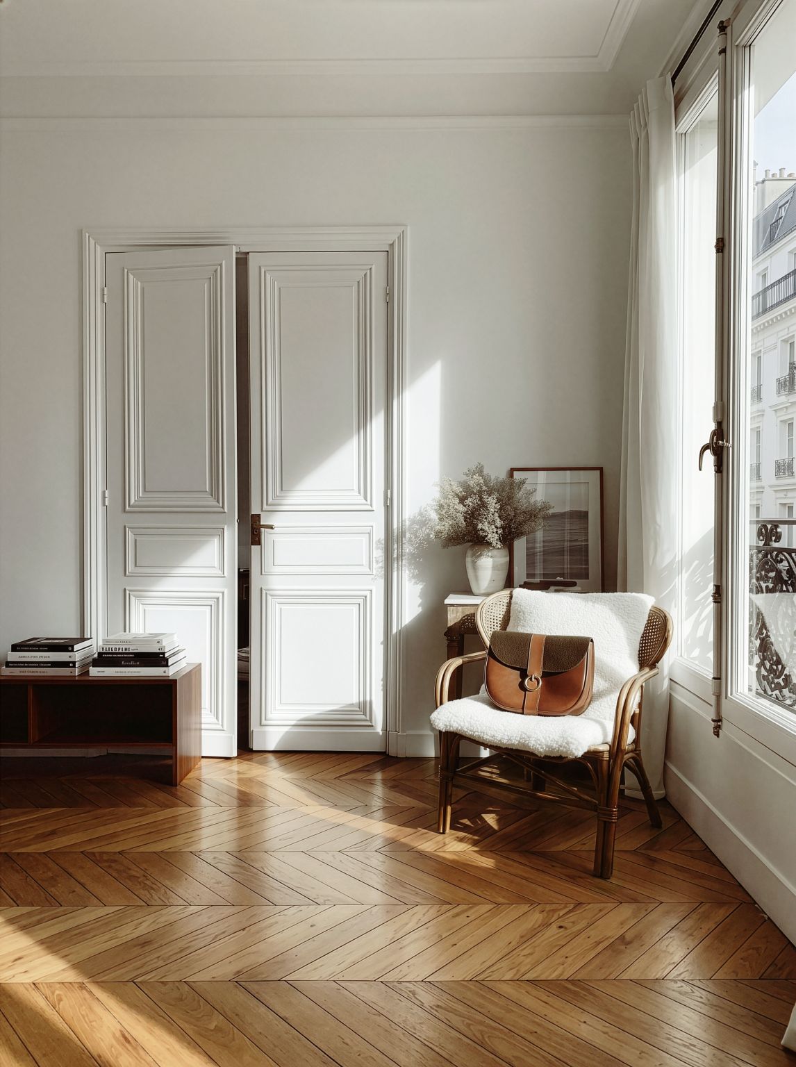 Sac à main en cuir marron posé sur un fauteuil en rotin, dans un salon haussmannien lumineux