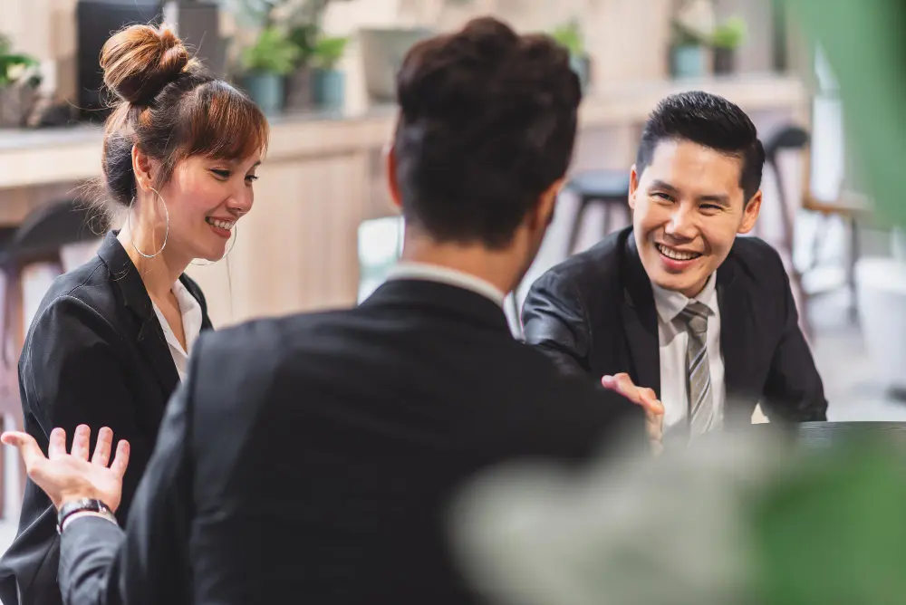 Colleagues smile and talk with each other across an office table
