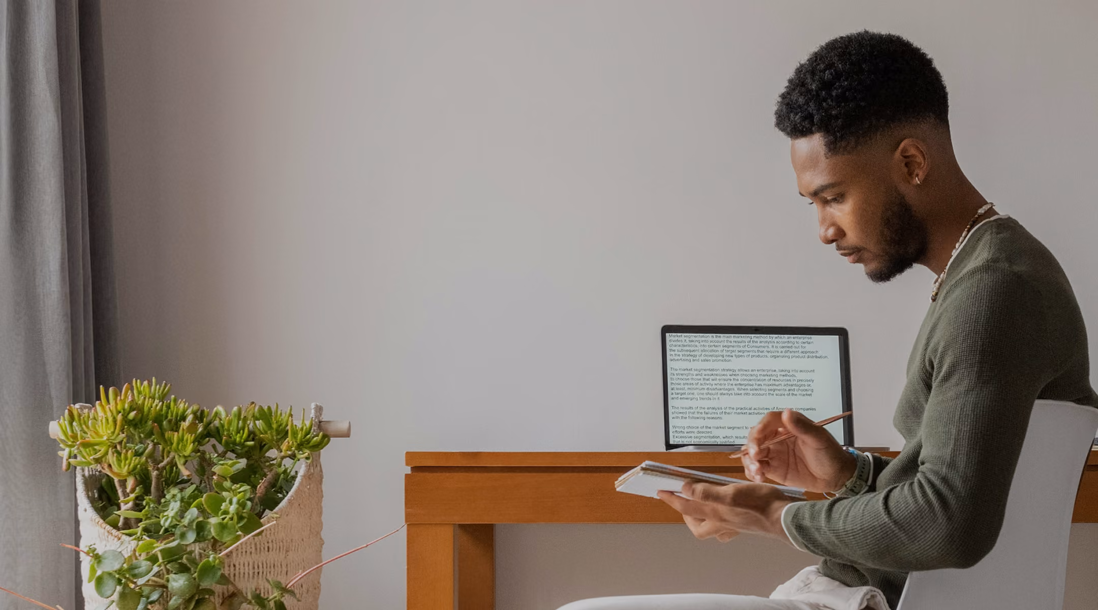 A man writes in a book sitting at his desk