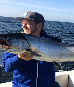 Man in a cap and blue jacket holding a large fish on a boat