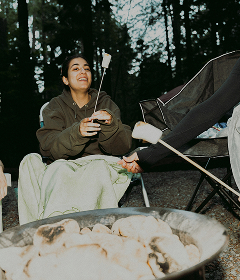 Smiling woman holding a roasting stick over a campfire at a campsite