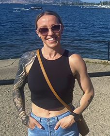Smiling woman in sunglasses and a black tank top standing beside the water