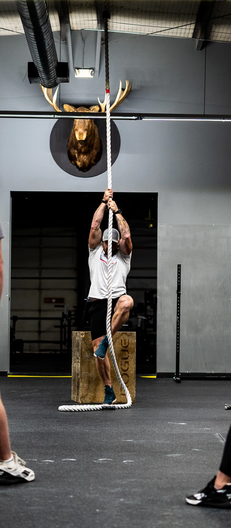 Compelled Fitness member doing a rope climb during a coached group class