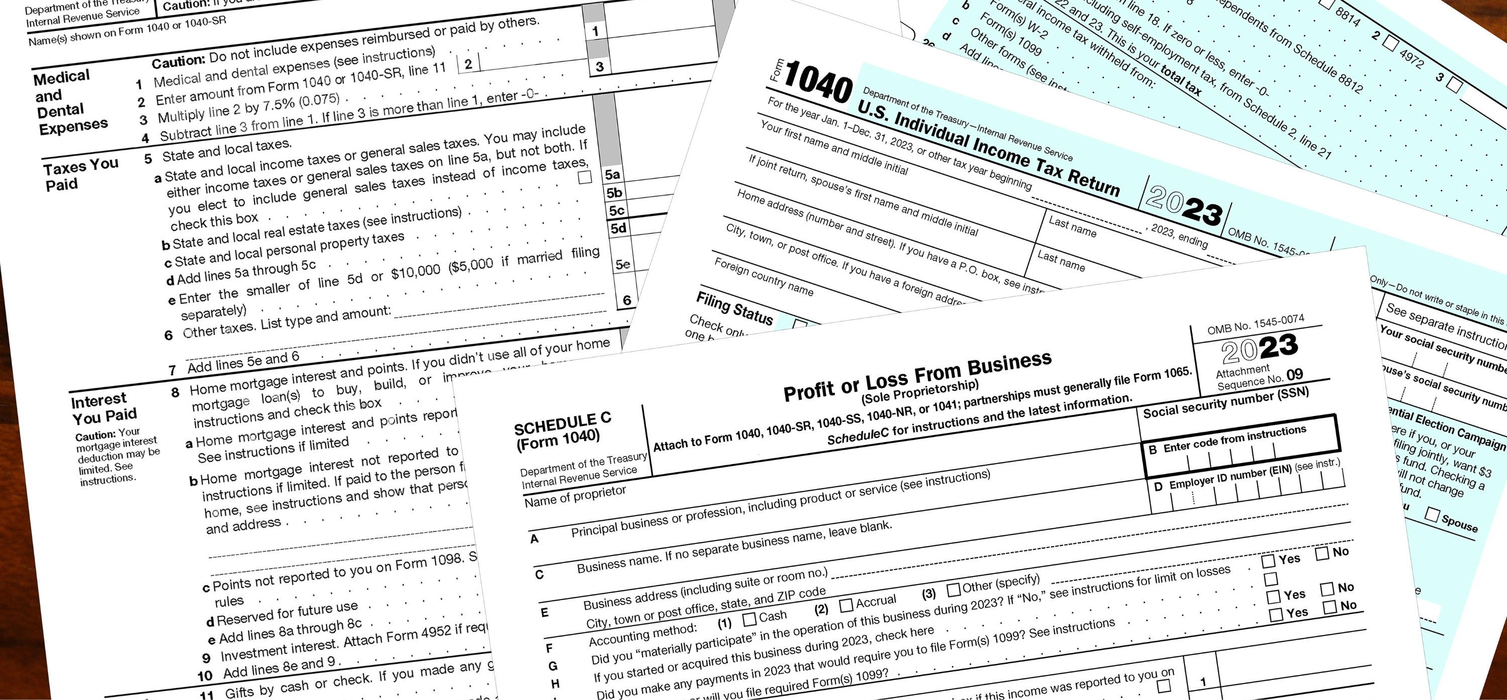 A stack of U.S. tax forms including Form 1040 for individual income tax return and Schedule C for profit or loss from business, partially visible with printed text and checkboxes on a wooden surface.