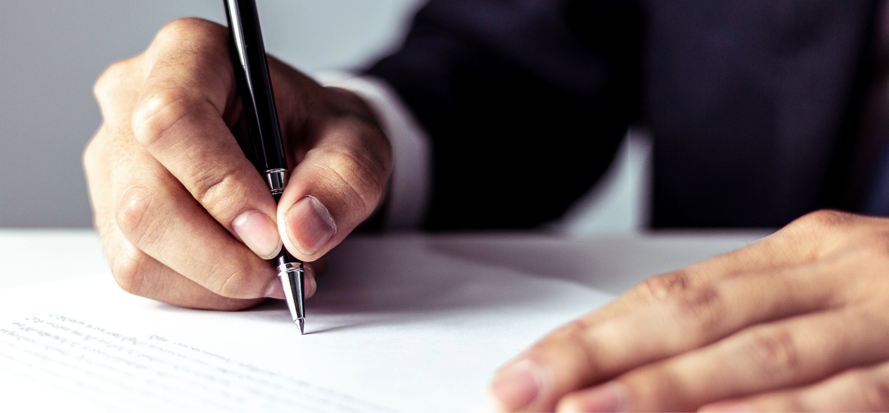 Close-up of a person's hand holding a black pen poised to write on a document with printed text, with another hand resting on the paper.