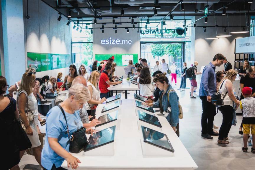Shoppers browsing shoes on tablet kiosks along a long counter in the eobuwie.pl store in Gdańsk