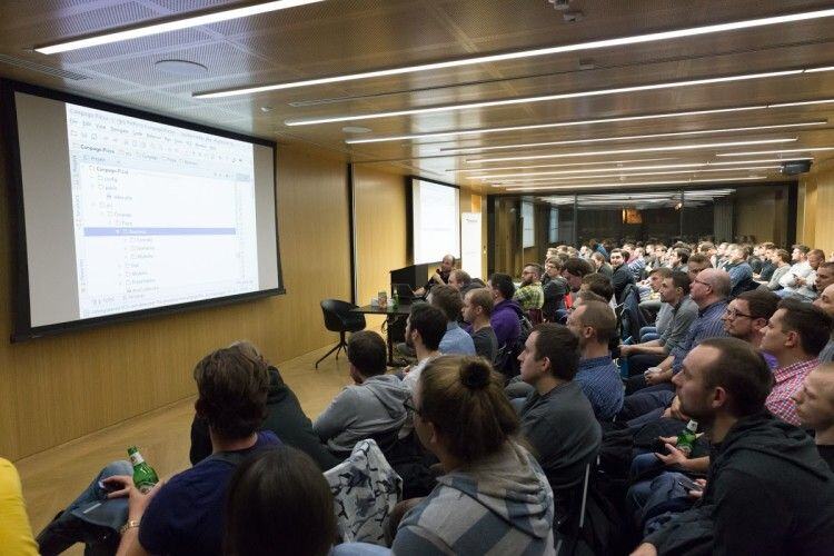 A packed room of developers watching a presentation with a code editor on screen at PHPers Poznań