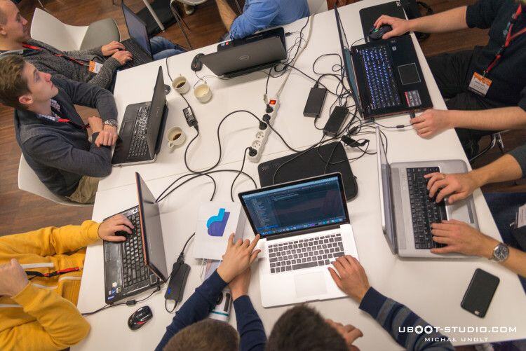 Overhead view of hackathon developers working on laptops around a shared table full of cables at Meet Magento Poland