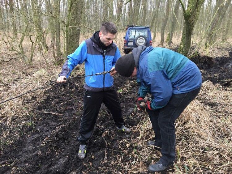 Two people in the forest mud handling a tow rope to pull out a 4x4