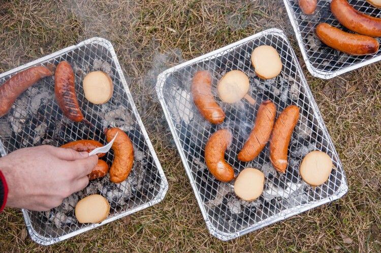 Kiełbasa sausages and bread grilling on disposable barbecues set on the grass