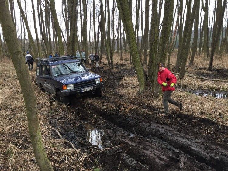 Blue Land Rover churning through a muddy forest track as a person in a red jacket walks alongside
