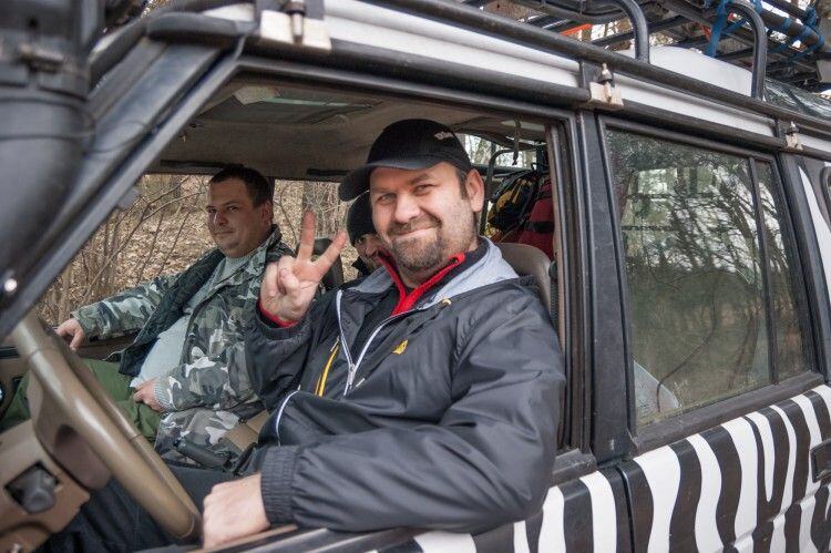 Grinning off-road guide giving a peace sign from the window of the zebra-striped Land Rover