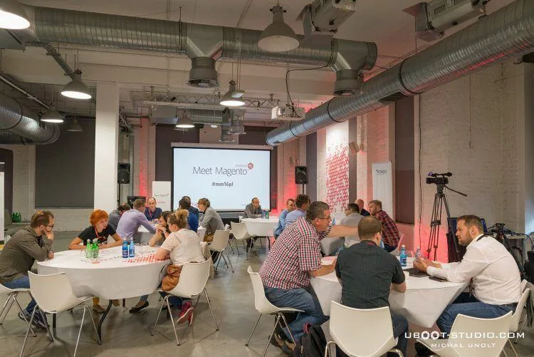 Round Table Session at Meet Magento Poland 2016, attendees talking around tables in front of a projector screen