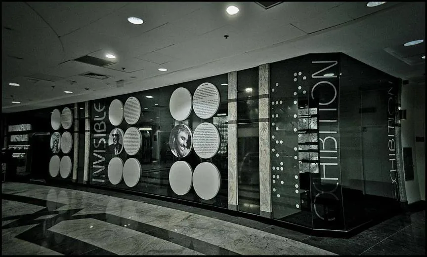 Entrance to the exhibition in a shopping centre, with INVISIBLE EXHIBITION lettering and braille-style dots on the glass