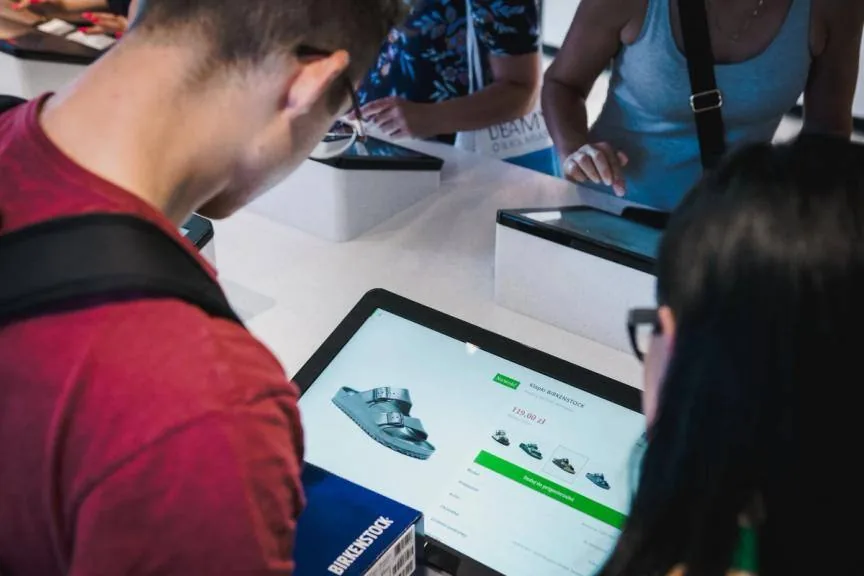 Shoppers using a tablet kiosk showing a Birkenstock sandal product page in the eobuwie.pl store