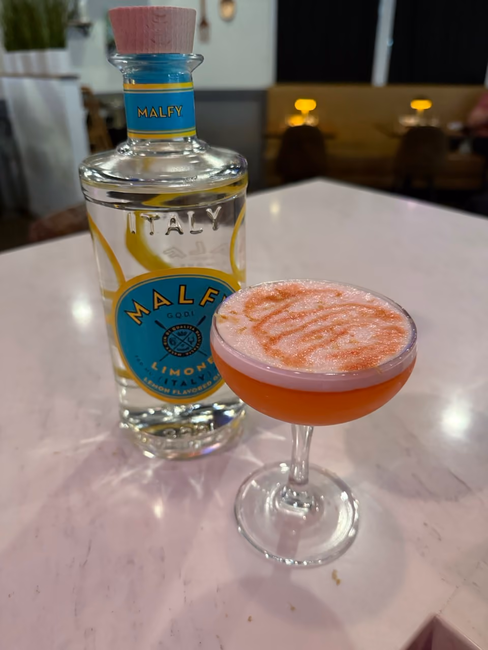A bottle of Malley sits next to a glass of pink drink.