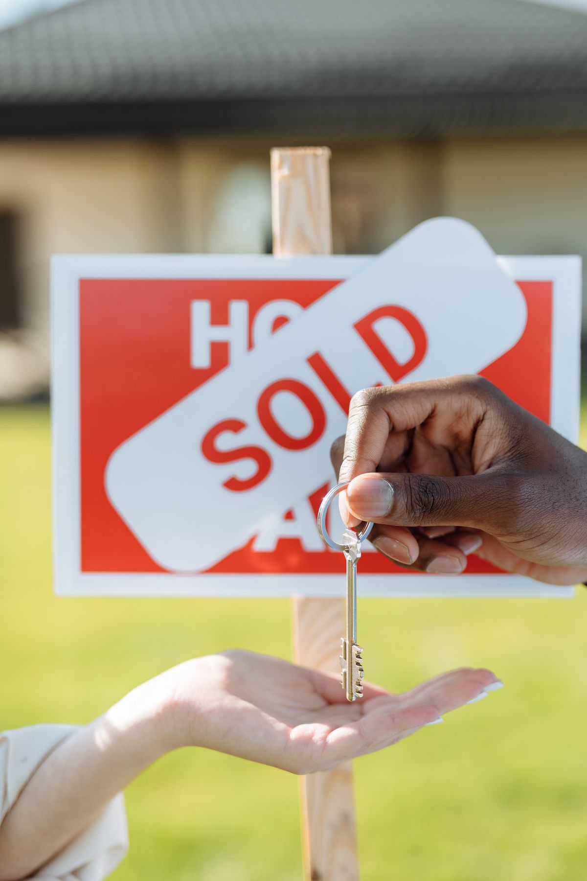 Close-up of hands exchanging a house key in front of a sold sign