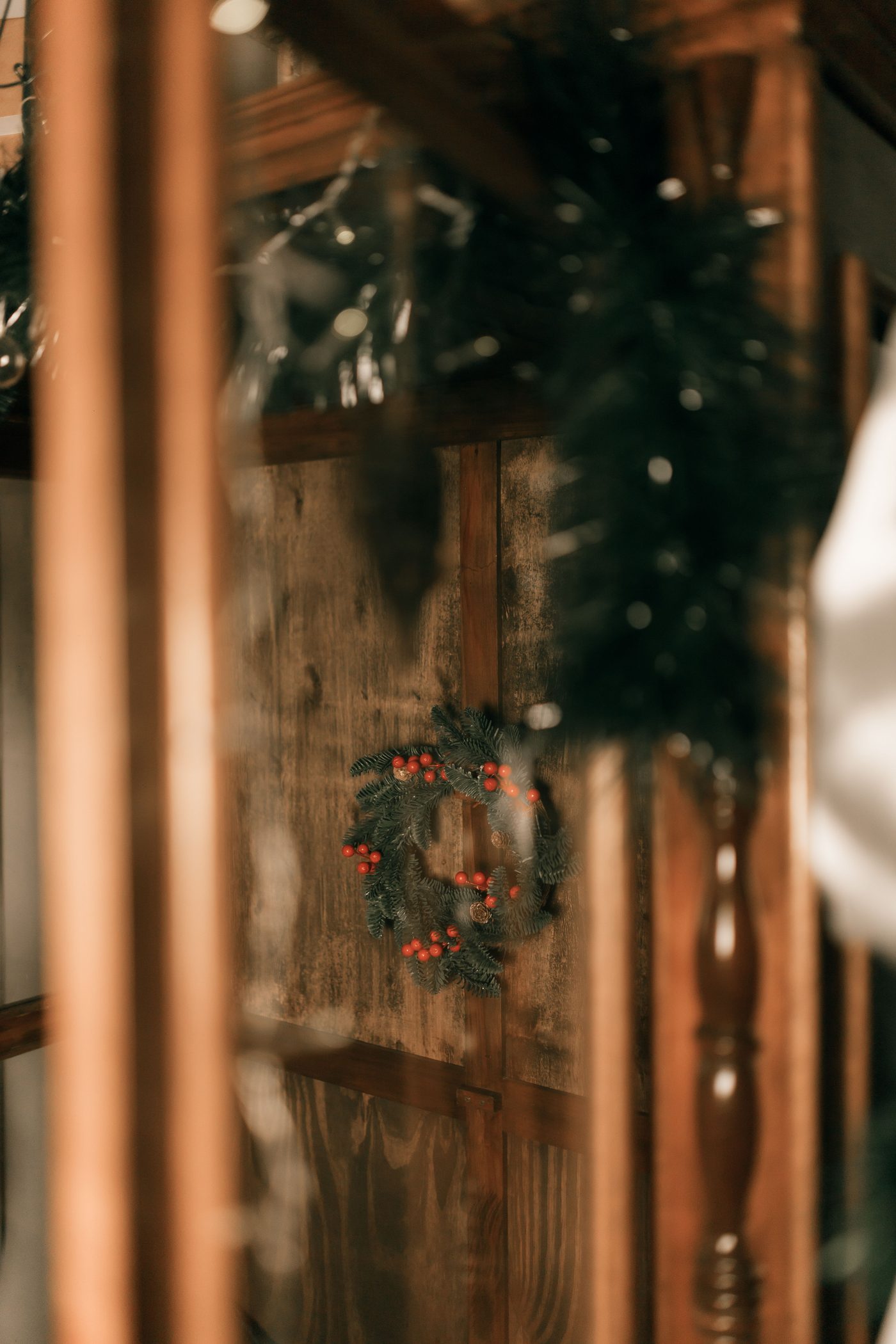 A small holiday wreath with red berries hanging on a wooden wall