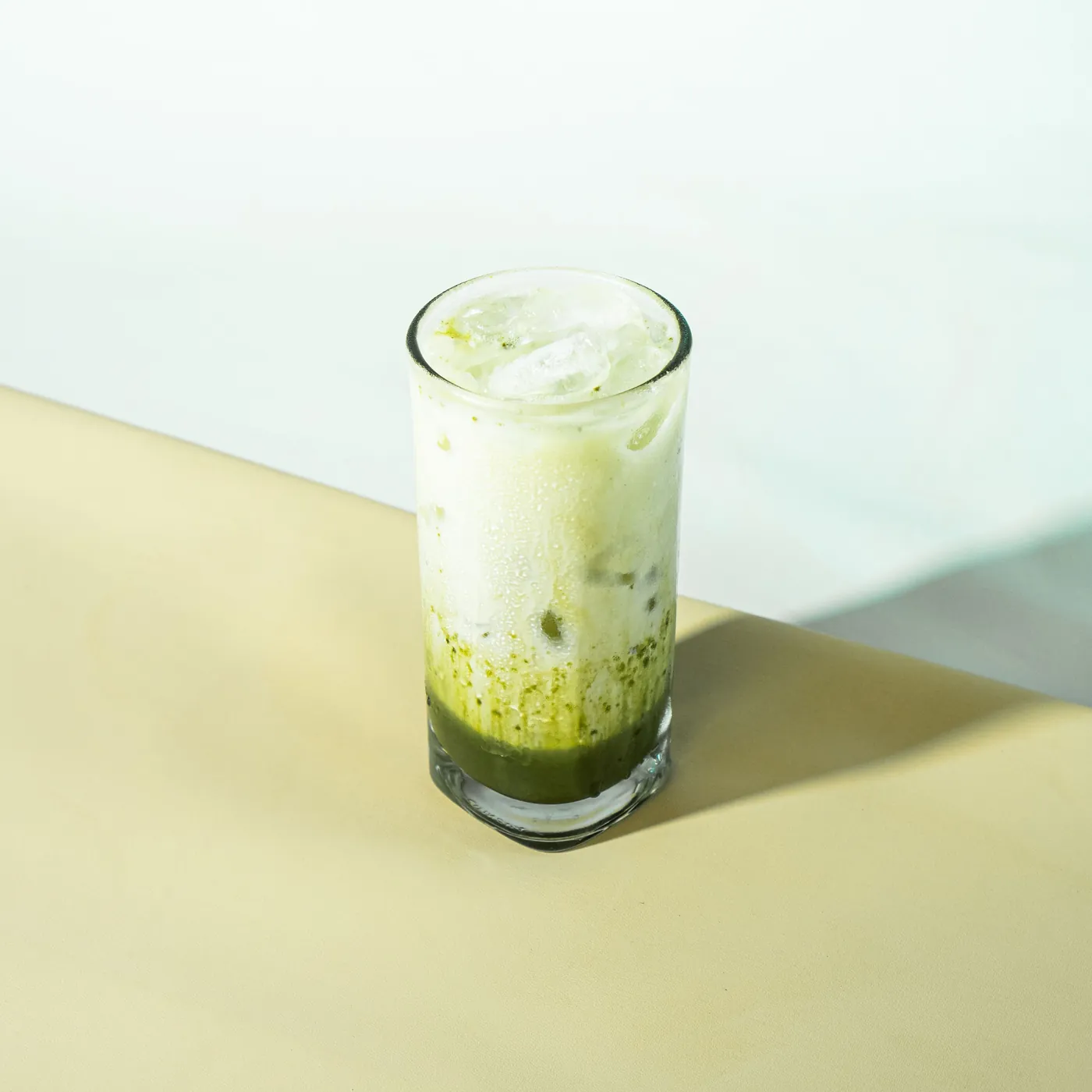 Iced matcha latte in a clear glass with a green matcha layer beneath milk and ice