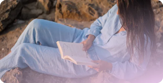 Une femme lit, assise sur des rochers au soleil