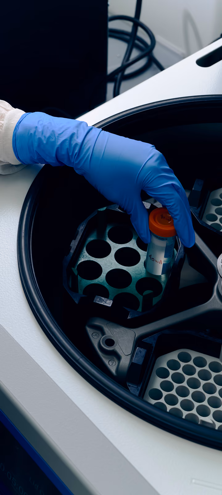 Gloved hands adding test tube to centrifuge