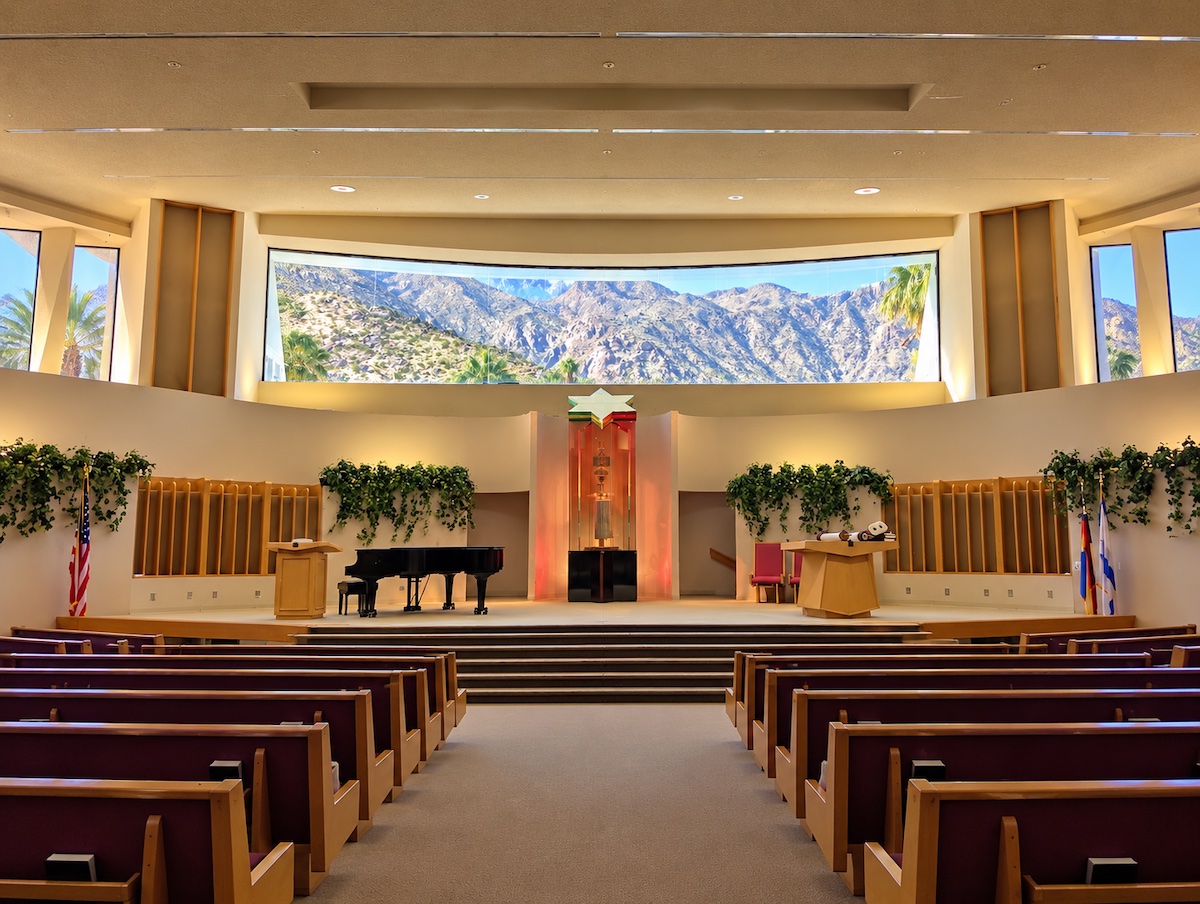 Sanctuary of Temple Isaiah in Palm Springs: rows of wooden pews face a raised bimah with a glowing Torah ark beneath a Star of David, and a wide window above frames the San Jacinto Mountains