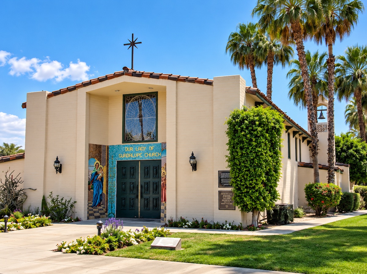 Our Lady of Guadalupe Catholic Church in Palm Springs: a cream stucco facade with a tile roofline and a cross above, a round stained-glass window, and a colorful mosaic framing the entrance doors, set among palm trees