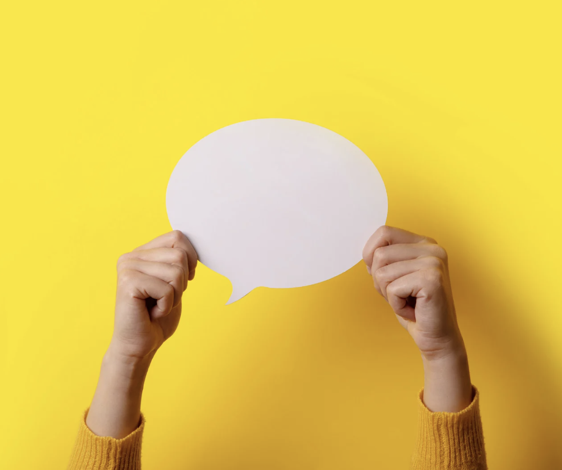 Hands holding blank white speech bubble against bright yellow background, symbolizing communication, messaging, or ideas.