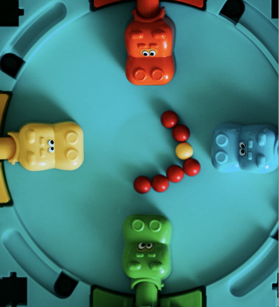 Colorful plastic hippo toys arranged around game board with marbles, representing a classic Hungry Hungry Hippos board game.