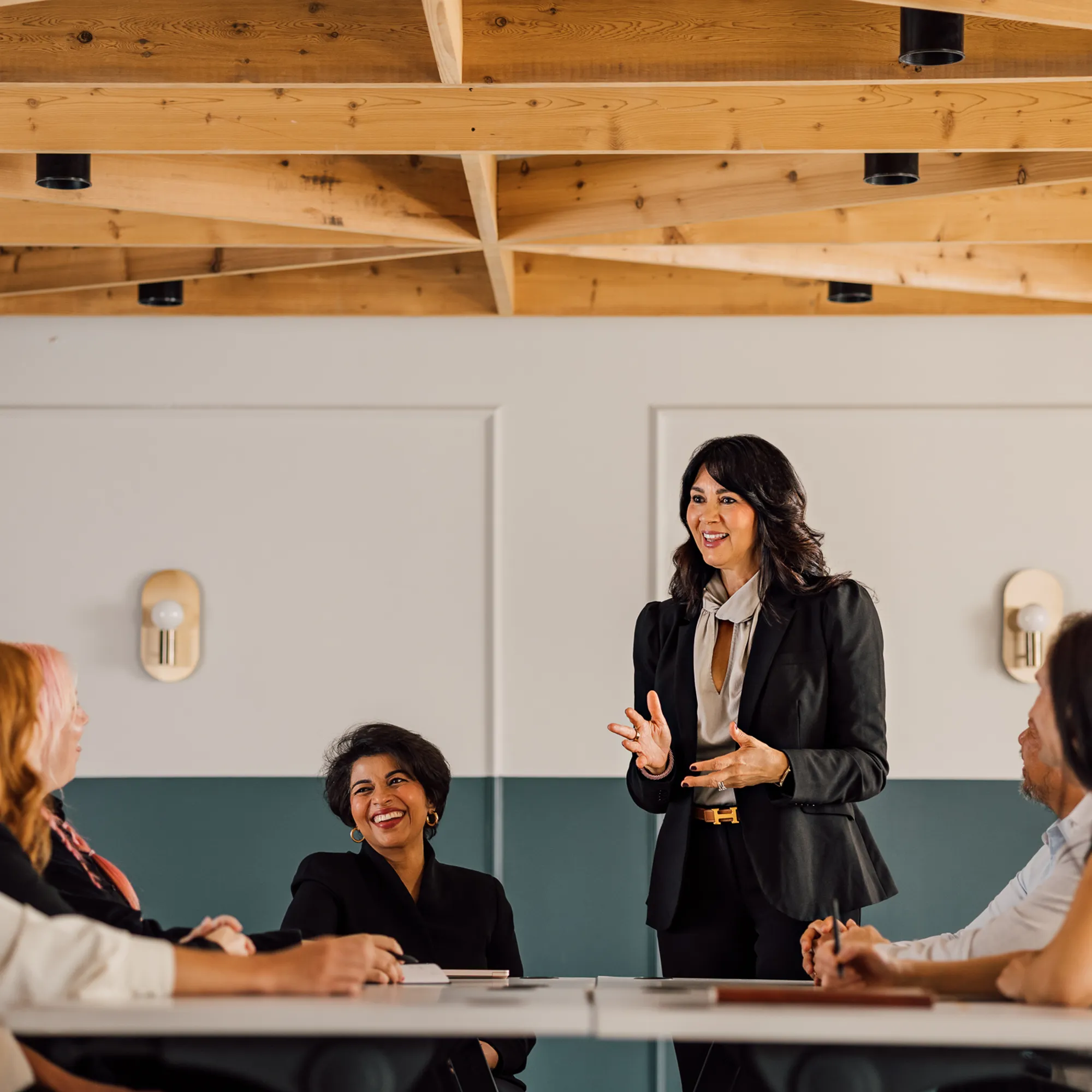 Facilitator speaks with animated gestures as participants around a table smile and listen