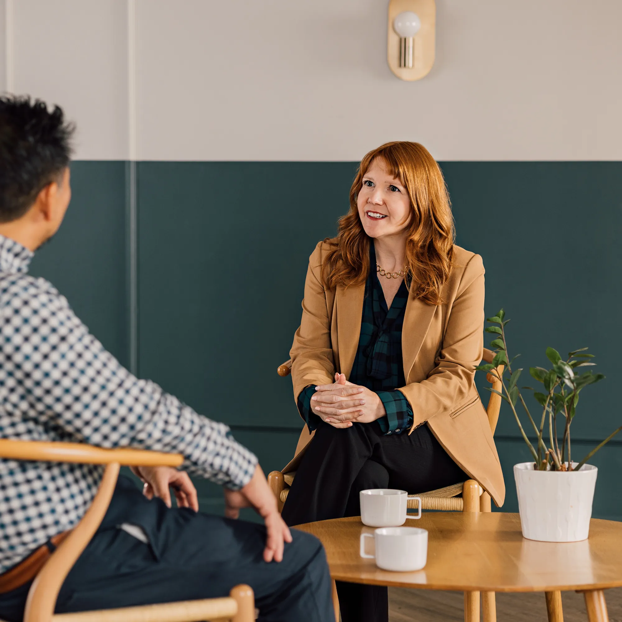 Woman in a blazer talks with a man over coffee in a relaxed coaching conversation