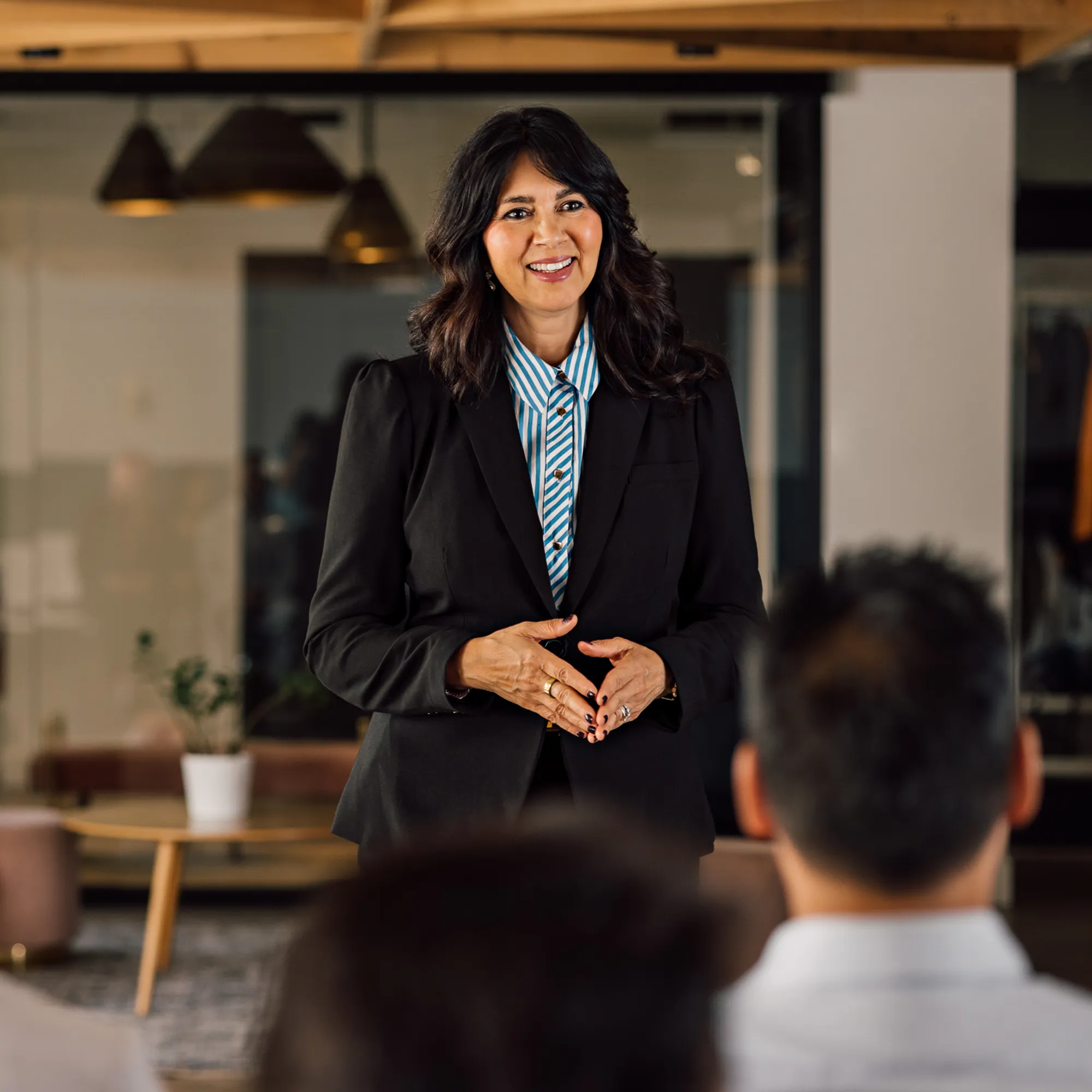 Smiling speaker in a black blazer and striped shirt addresses a seated audience