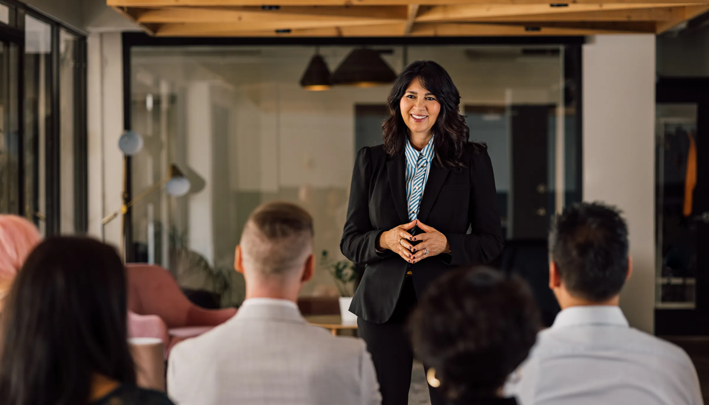 Speaker in a black blazer smiles at an audience seated in a modern event space