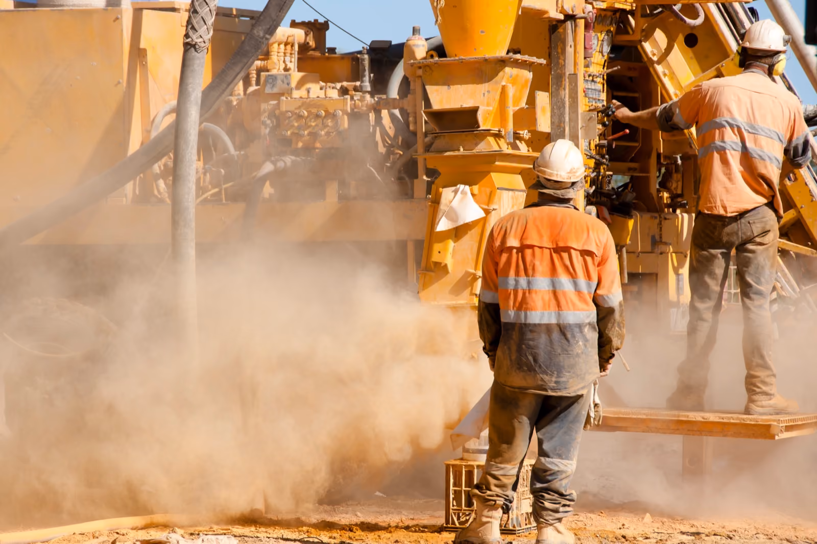 Mine site workers beside heavy machinery in dust