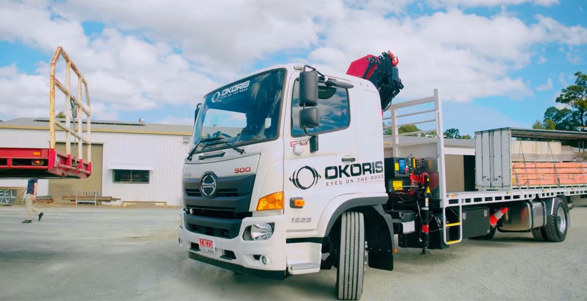 OKORIS-branded flatbed truck with a crane, parked in a depot yard