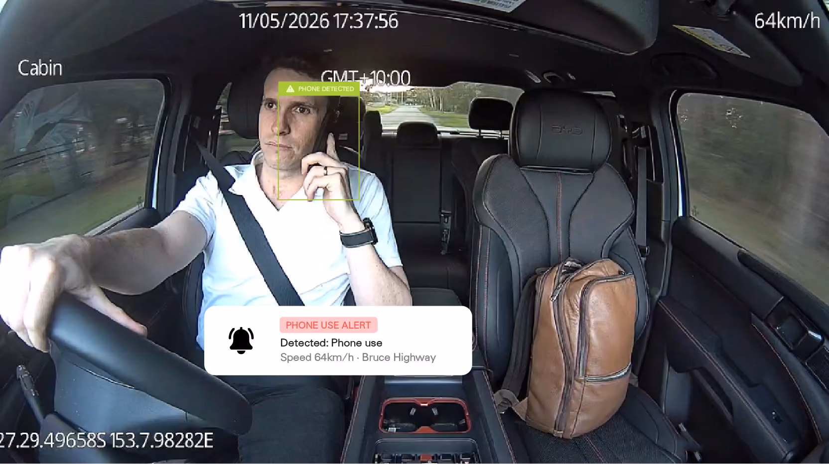 In-cab camera view with a phone-use alert: the driver is detected holding a phone at 64km/h on the Bruce Highway