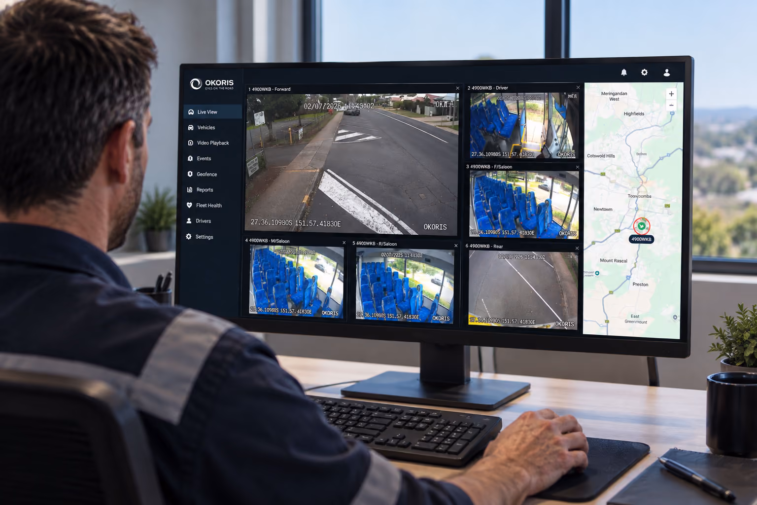Fleet manager at a desk viewing the OKORIS live view with six bus camera feeds and a route map