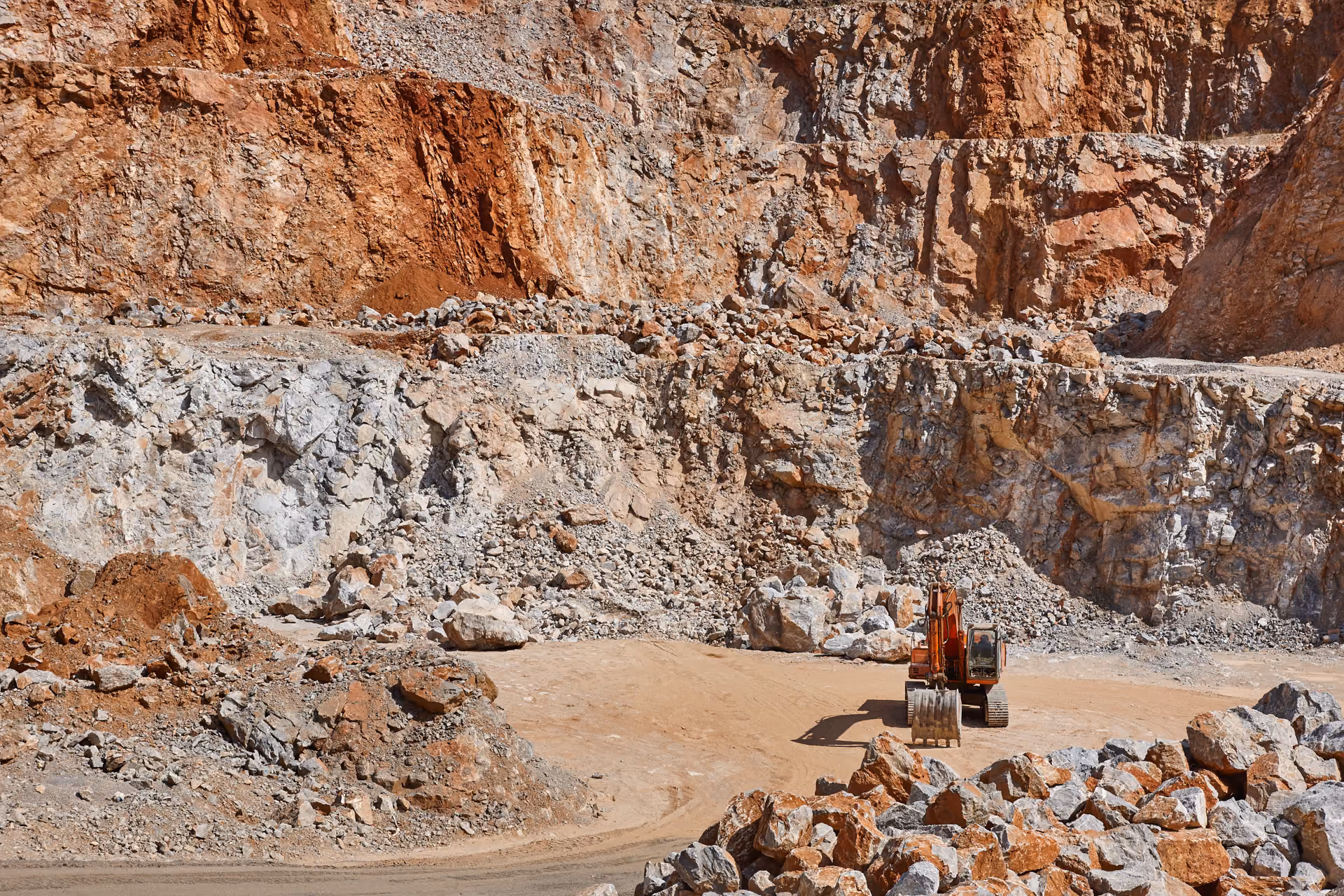 Excavator working at the base of an open-cut quarry wall