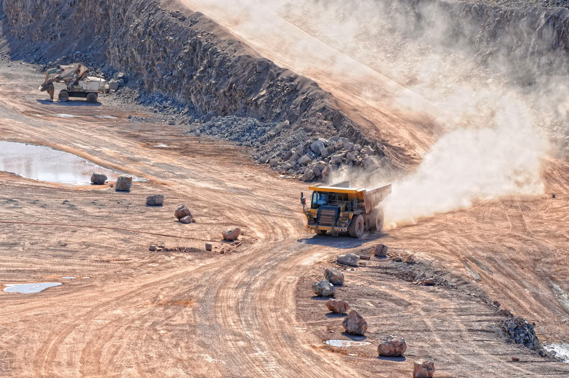 Haul truck raising dust on a quarry access road with an excavator on the bench above