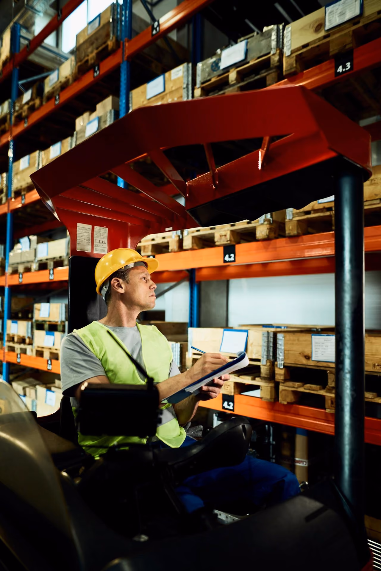 Forklift operator in high-vis completing a checklist beside warehouse racking