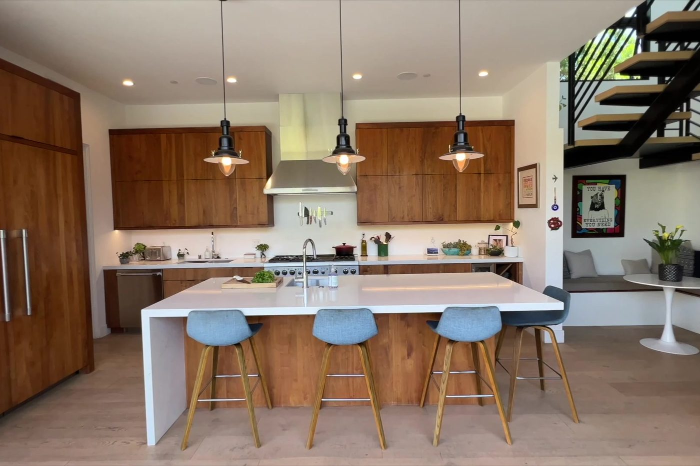 The Modern Monica kitchen: wood cabinets, a waterfall island with stools and pendant lights.