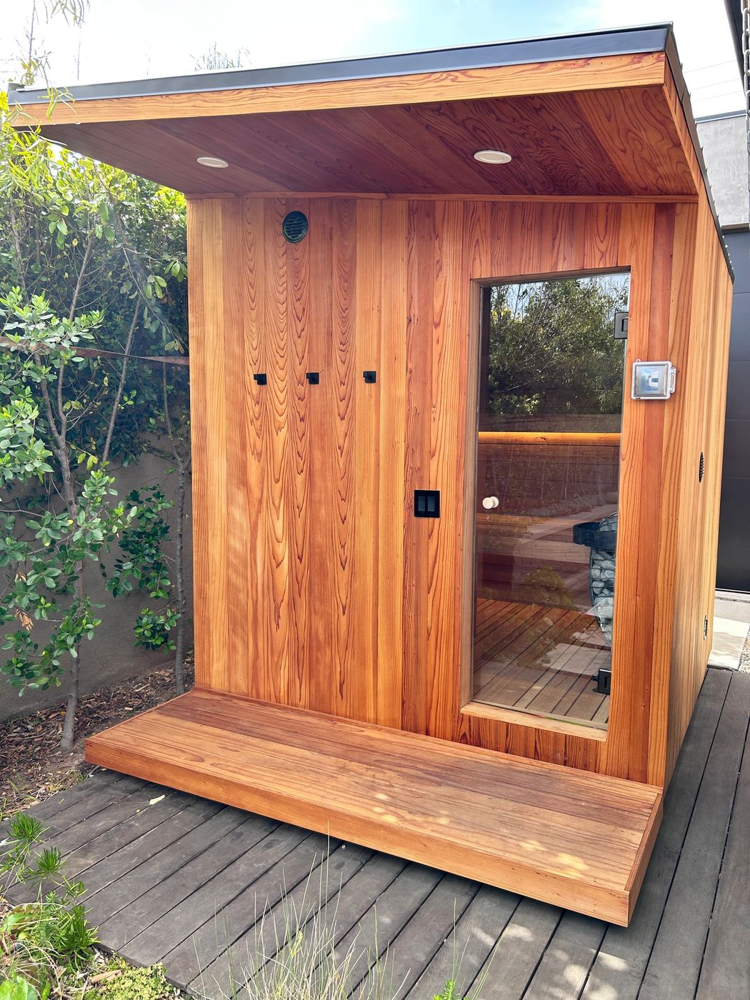 Redwood sauna exterior with a covered roof, a glass door and a redwood deck