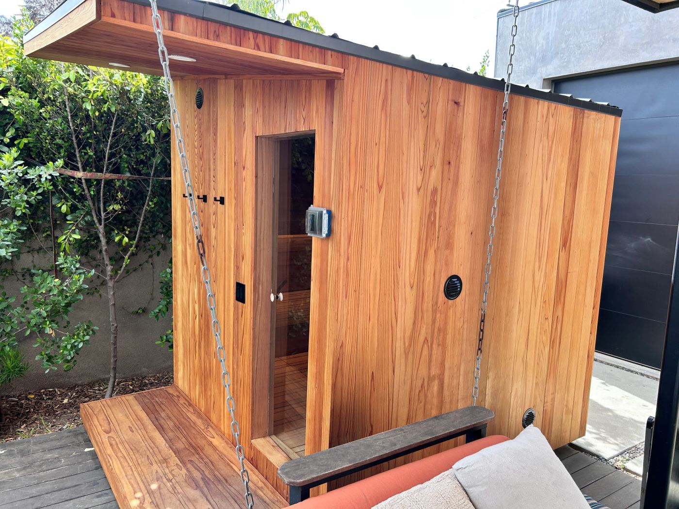The redwood sauna from the side, with a swing bench on the deck