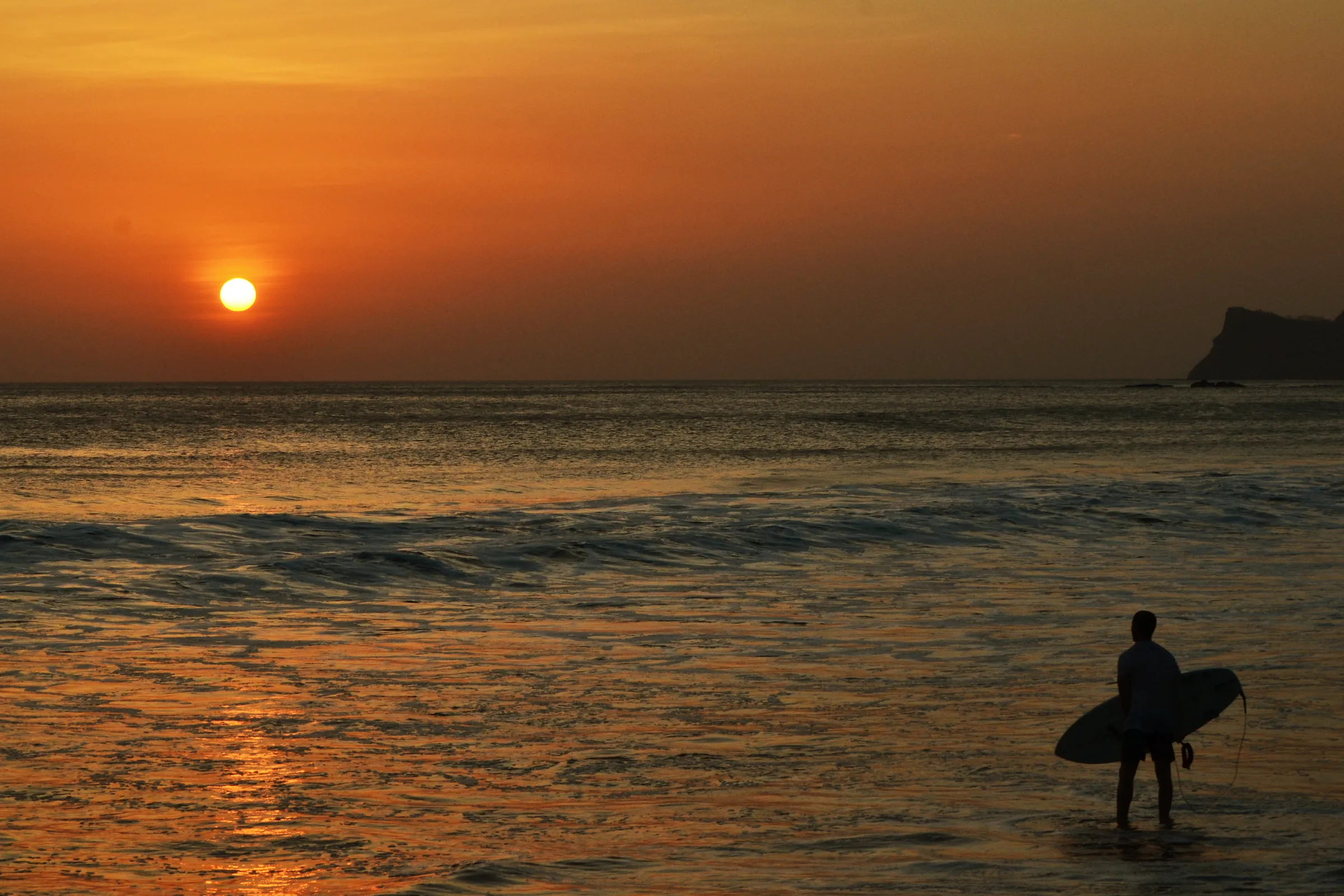 Surfer silhouetted beside the ocean at sunset