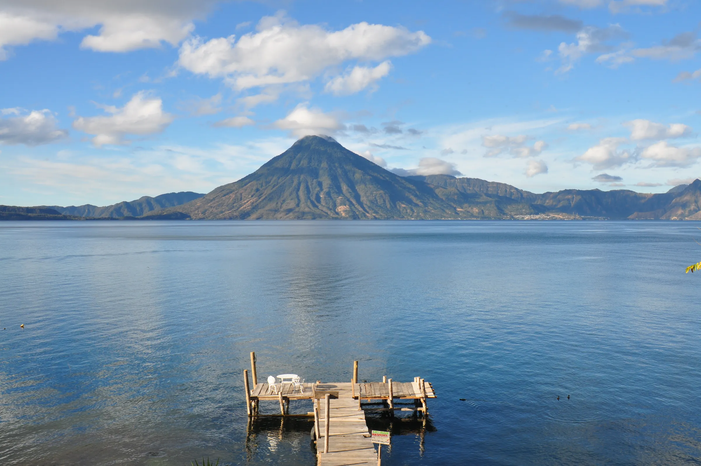 A wooden dock stretches across Lake Atitlán toward a volcanic peak.
