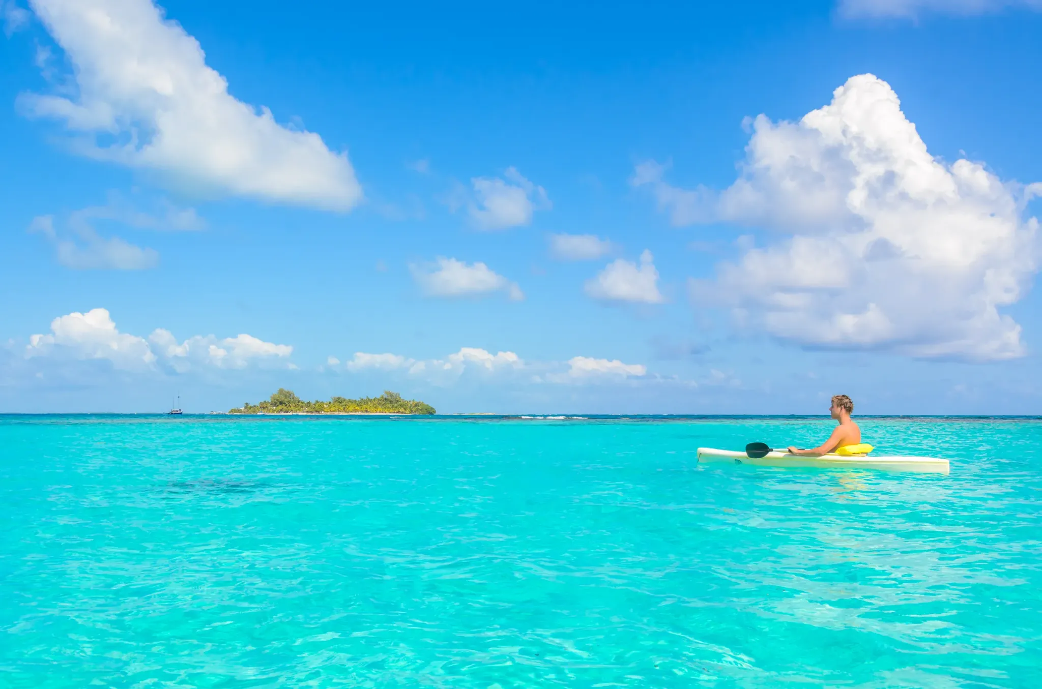 Kayaker on turquoise water near a caye, Belize