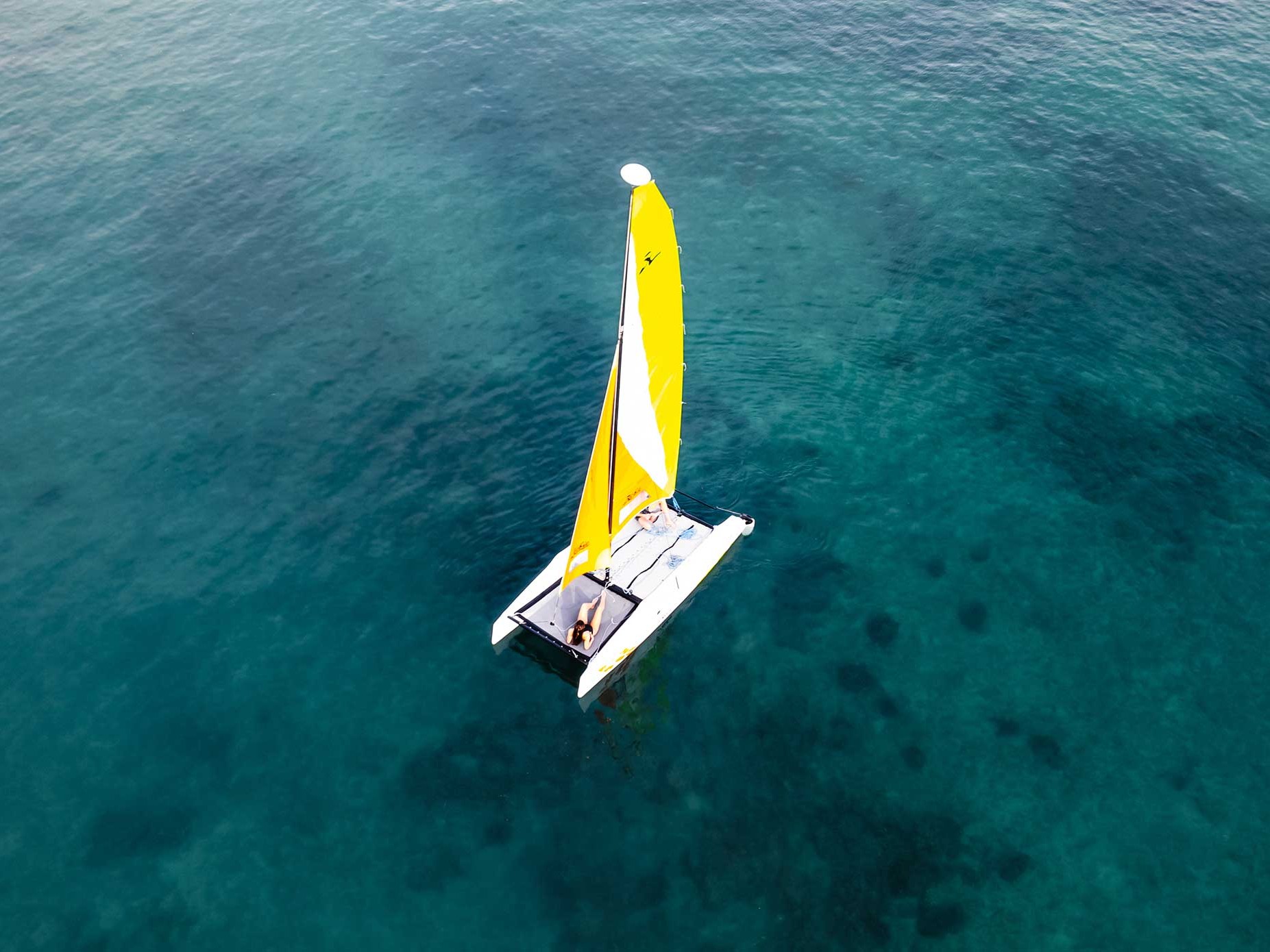 Aerial view of a small catamaran with a yellow sail drifting over turquoise waters near Islas Secas, Panama.